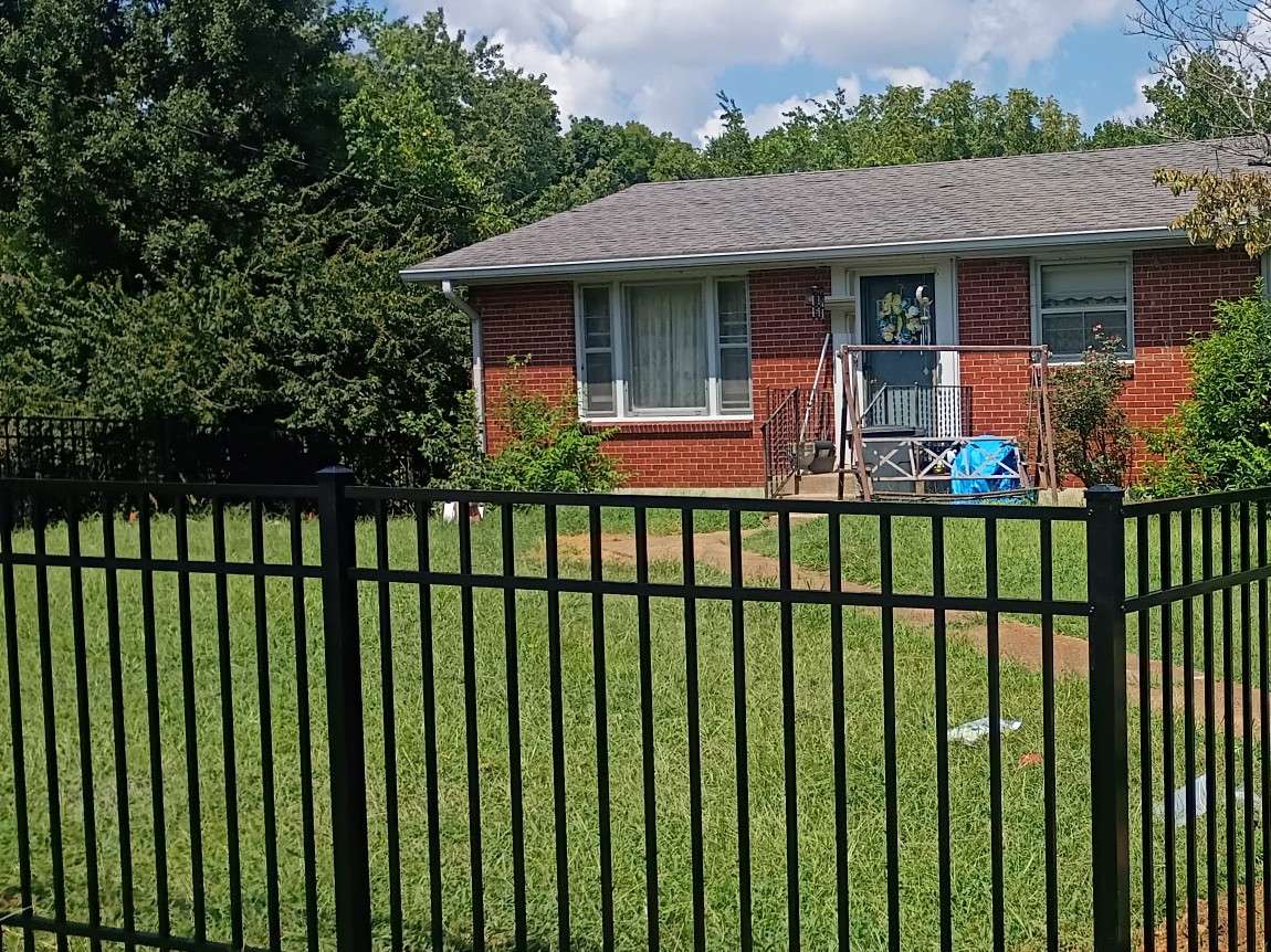 Black metal picket fence around the front yard of a red brick ranch house