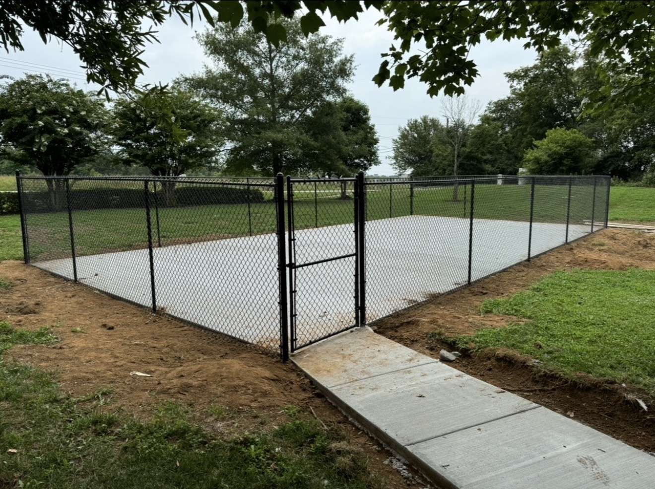 Black chain link fence with a walk gate around a new concrete court, with a sidewalk leading to the gate