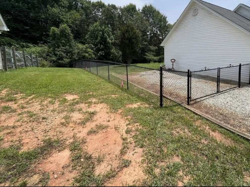 Black chain link fence along a yard with a double drive gate across a gravel driveway