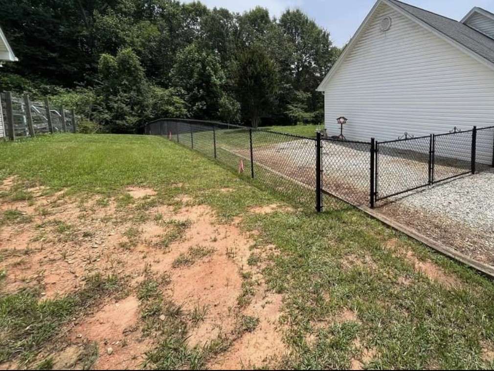 Black chain link fence along a yard with a double drive gate across a gravel driveway