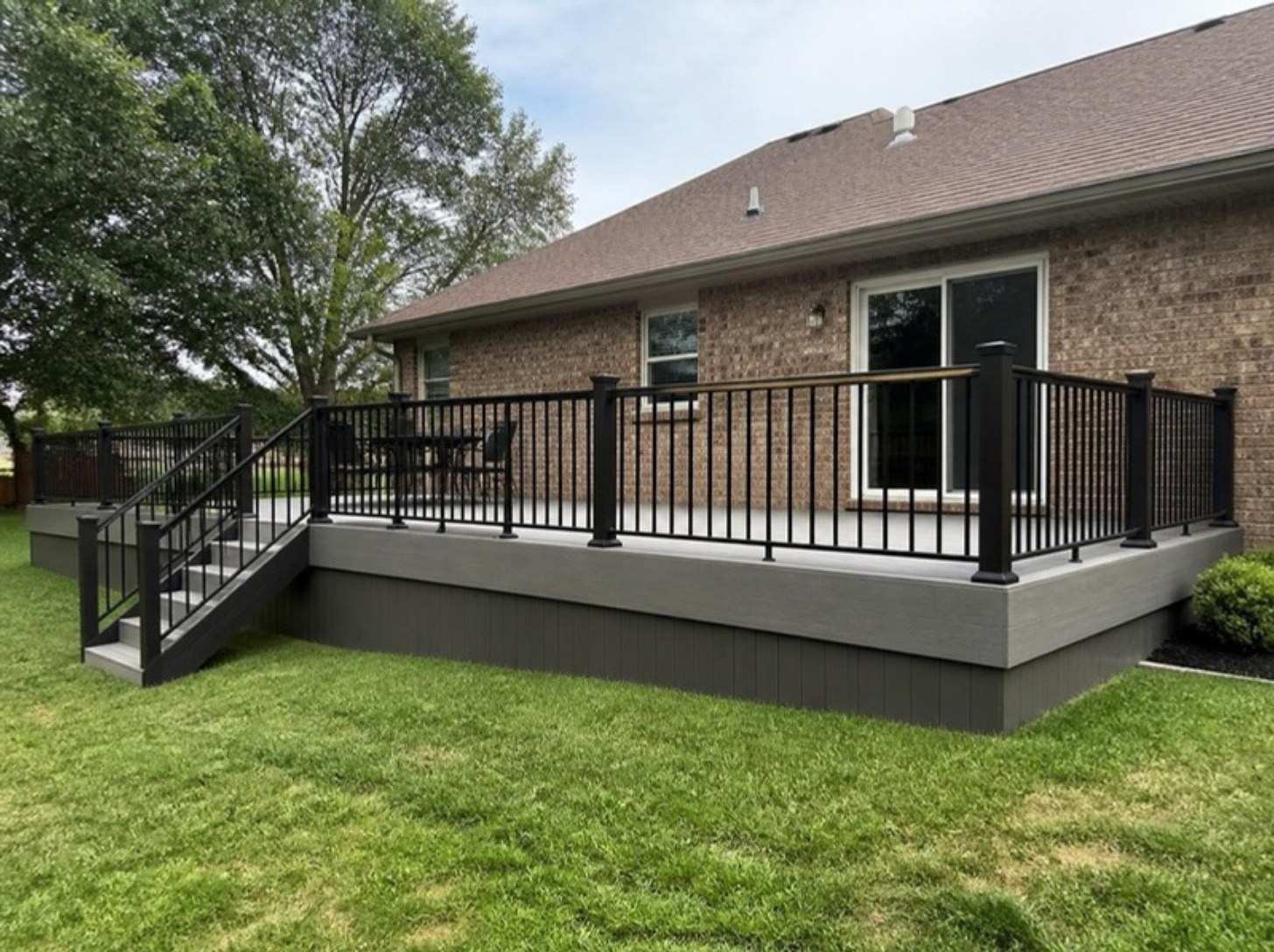 Gray composite deck with black metal railings behind a brick house