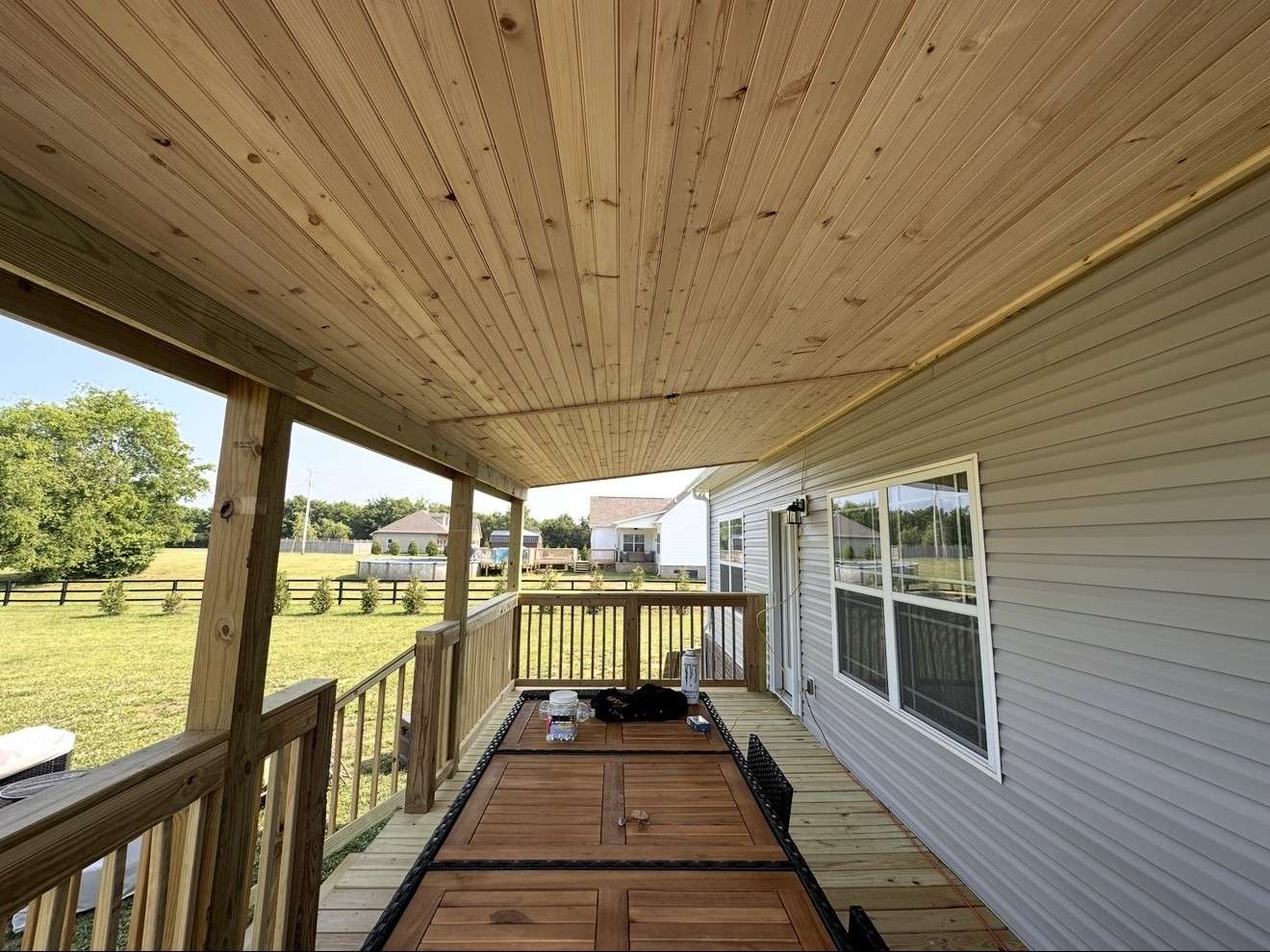 View along a covered deck with a tongue and groove wood ceiling, wood railings, and a view of open fields