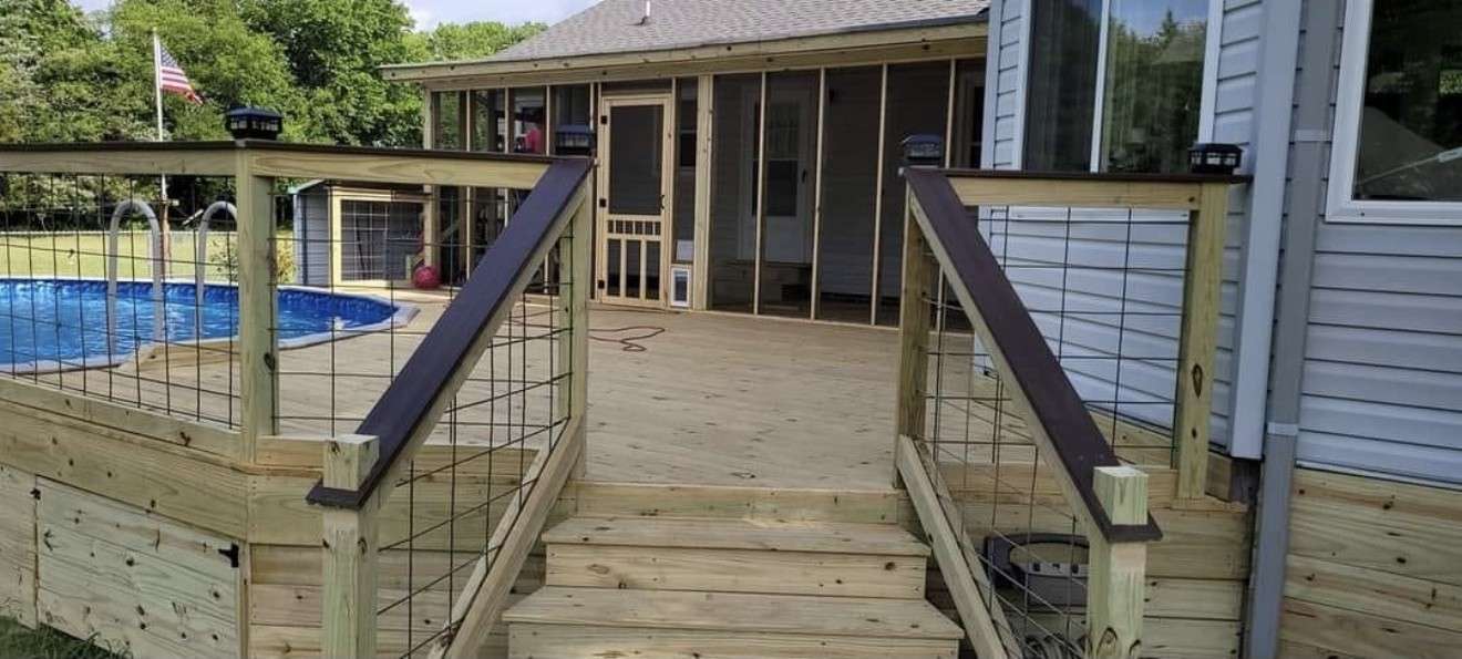 New pressure treated deck with wire panel railings, dark handrails, and wide steps, beside an above ground pool