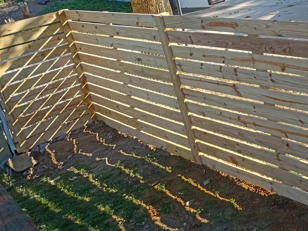 New horizontal board fence in pressure treated pine running from the corner of a house and turning along the side yard