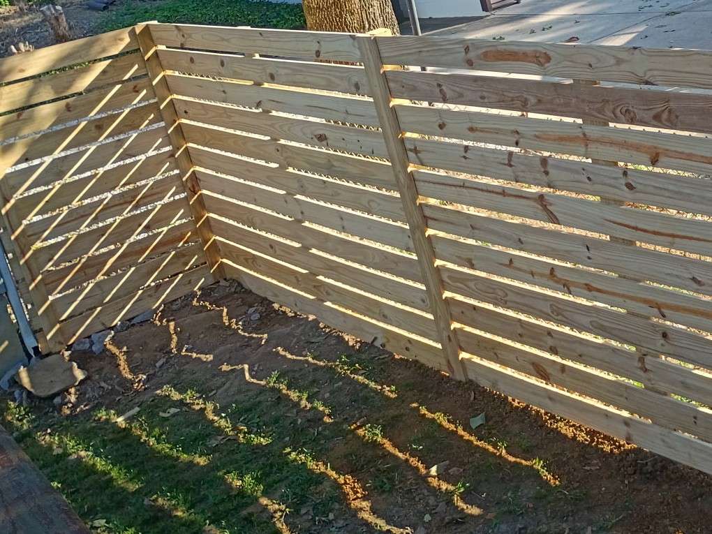 New horizontal board fence in pressure treated pine running from the corner of a house and turning along the side yard
