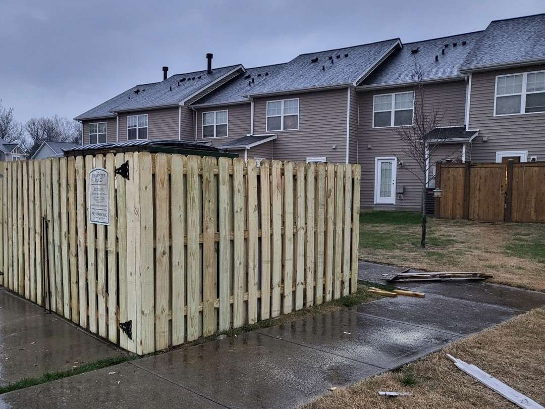 New shadowbox style wood fence with gates enclosing a dumpster at a townhome community