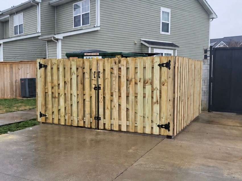 New shadowbox style wood enclosure with double gates and black strap hinges around a dumpster at a townhome community