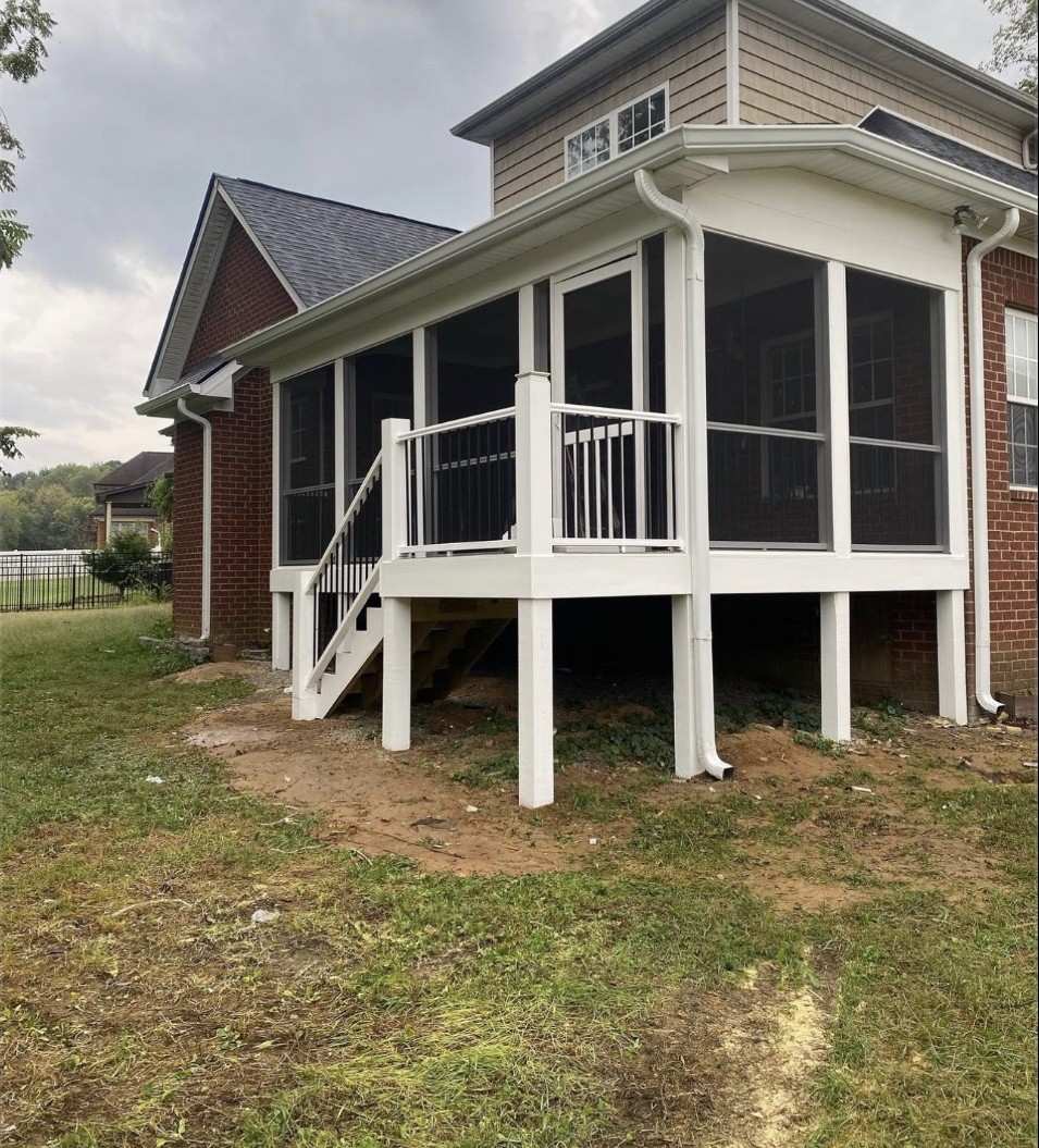 Raised white deck with a railing and stairs on tall posts, on the back of a brick house