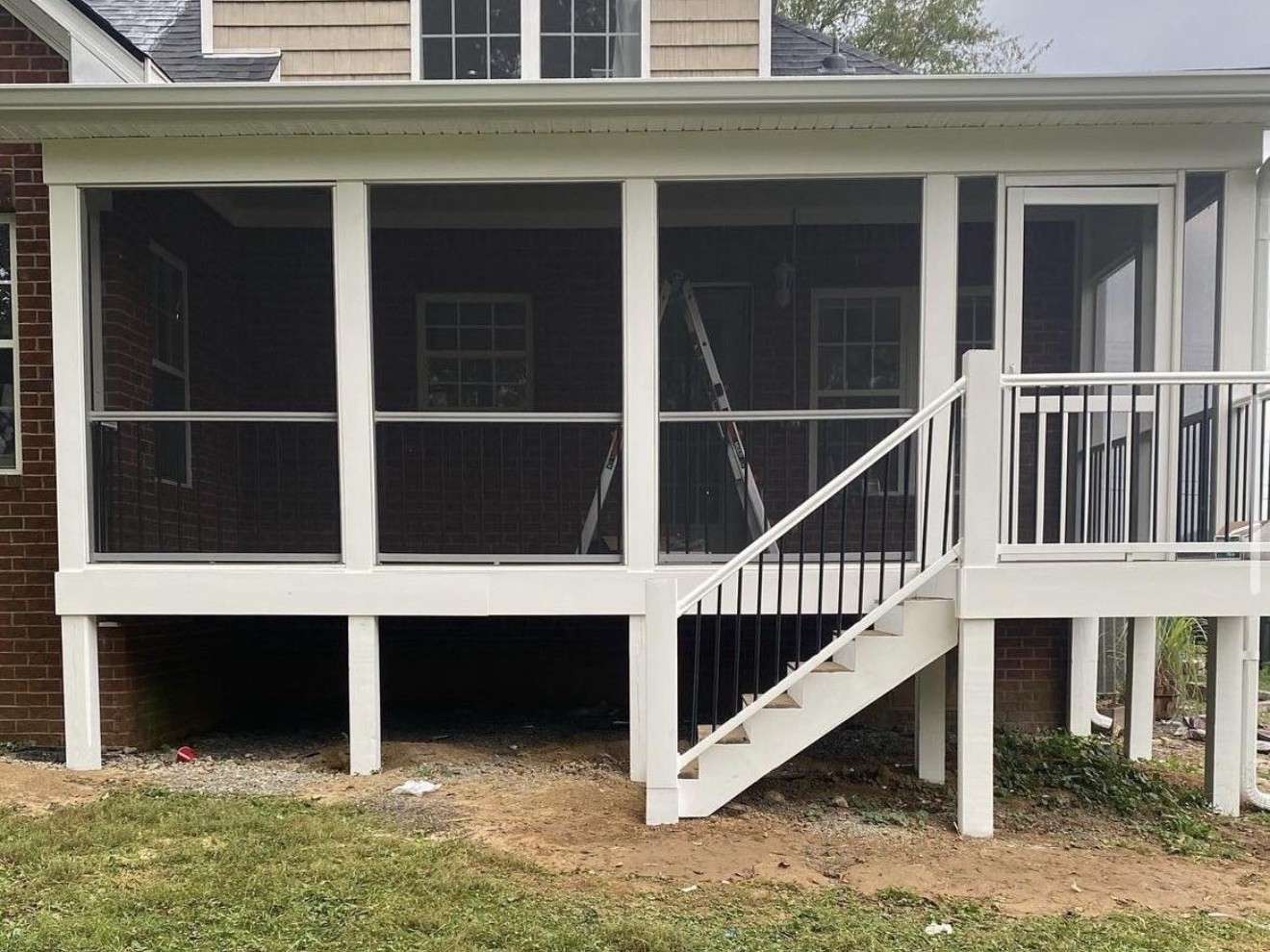 White painted raised deck with stairs and black balusters on the back of a brick house