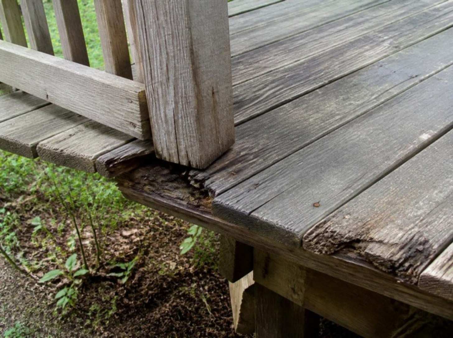 Close view of an old gray deck with cracked boards and a rotted board end under a railing post